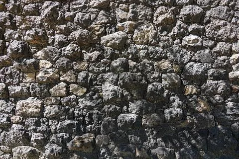 Rustic stone wall texture made of dark volcanic rocks with natural sunlight.. Fotos Stock