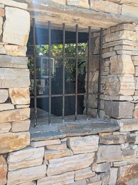 Rustic stone window with iron bars set in weathered masonry and sunlight Stock Photos