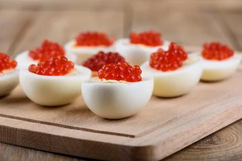 Rustic style. Red caviar on halves of hard-boiled chicken eggs on a cutting b Stock Photos