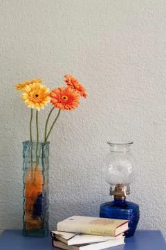 Rustic table with vase with orange and yellow flowers and old lamp and books Stock Photos