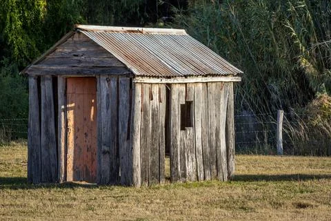 A rustic timber cabin stands weathered and worn in a quiet rural landscape. Stock Photos