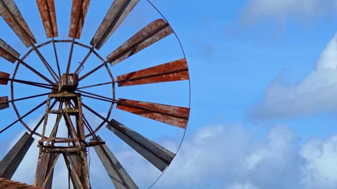 Rustic vintage wind pump spinning against blue sky and clouds Stock Footage 347448909