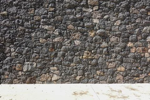 Rustic volcanic rock wall texture with a smooth concrete ground surface in .. Foto stock