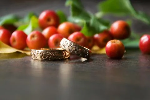 Rustic wedding decorations. Red small apples and gold rings on a wooden backg Stock Photos