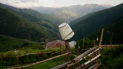 Rustic white bucket on a wooden post with a lush green mountainous backdrop in a Stock Footage 265499290