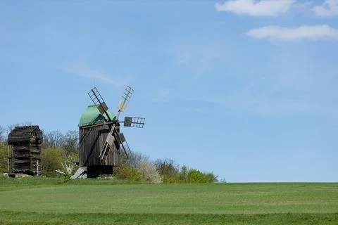 Rustic Windmill Amidst Green Fields Under Blue Sky Stock Photos