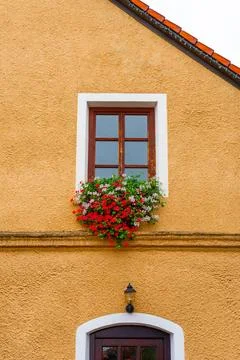 Rustic window with red and white blooming flowers on ochre stucco wall of Stock Photos