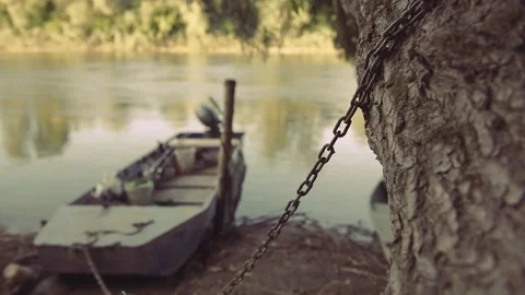 Rustic wooden boat chained to a tree by the river Stock Footage 135473656