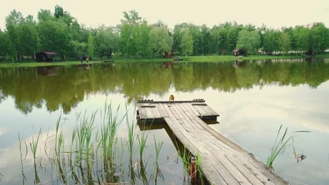 A rustic wooden bridge extends over a peaceful lakeside, perfect for fishing Video stock 204799178