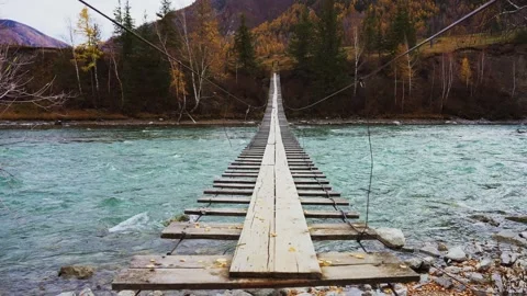 Rustic wooden bridge spans over a clear, rushing river Stock Footage 342736856