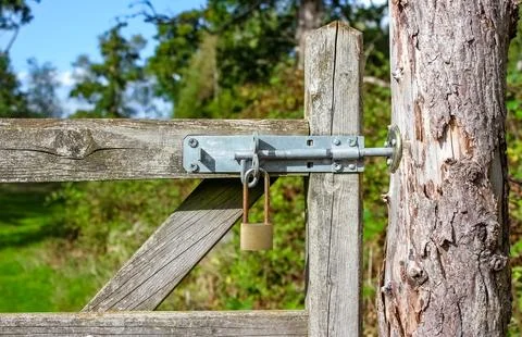 A rustic wooden gate secured with a heavy-duty metal slide bolt and a weather Stock Photos