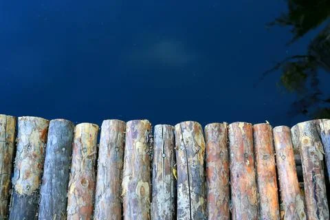 Rustic wooden logs form a border against deep blue water surface Foto stock