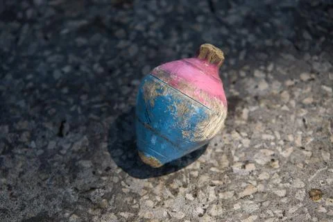 Rustic wooden spinning top painted in blue and pink on stone pavement Stock Photos