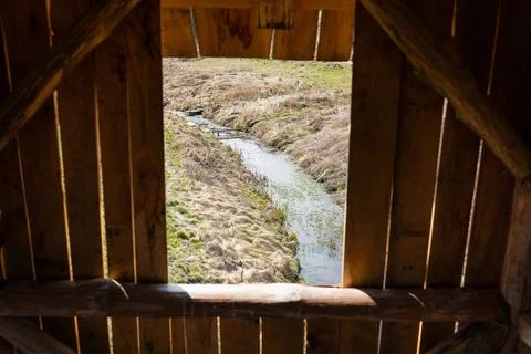 A rustic wooden structure frames a view of a tranquil stream flowing throug.. Stock Photos
