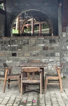A rustic wooden table and chairs gather on a cobblestone patio, framed by a.. Stock Photos