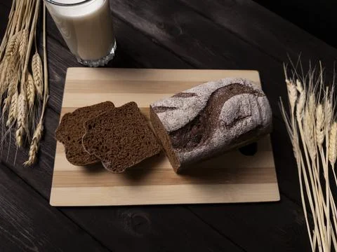 A rustic wooden table features a loaf of dark rye bread Stock Photos