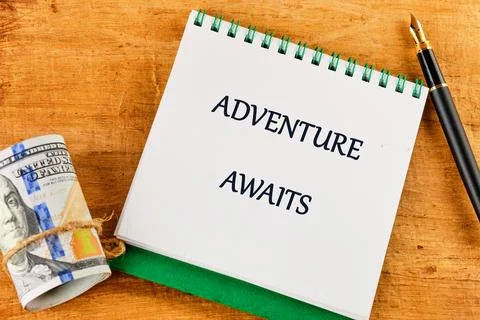 On a rustic wooden table, a notepad features the phrase adventure awaits, paired Stock Photos