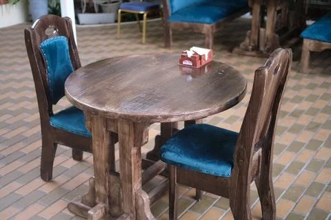 Rustic wooden table with two chairs featuring blue velvet cushions in a caf.. Stock-Fotos