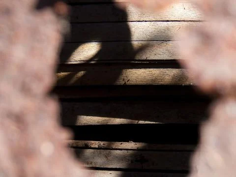 A rustic wooden wall seen through the hole of a rusted metalic plate, capture Stock Photos