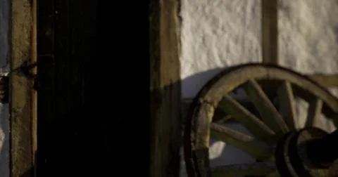 Rustic wooden wheel next to an old door reveals village charm at sunset Stock Illustration