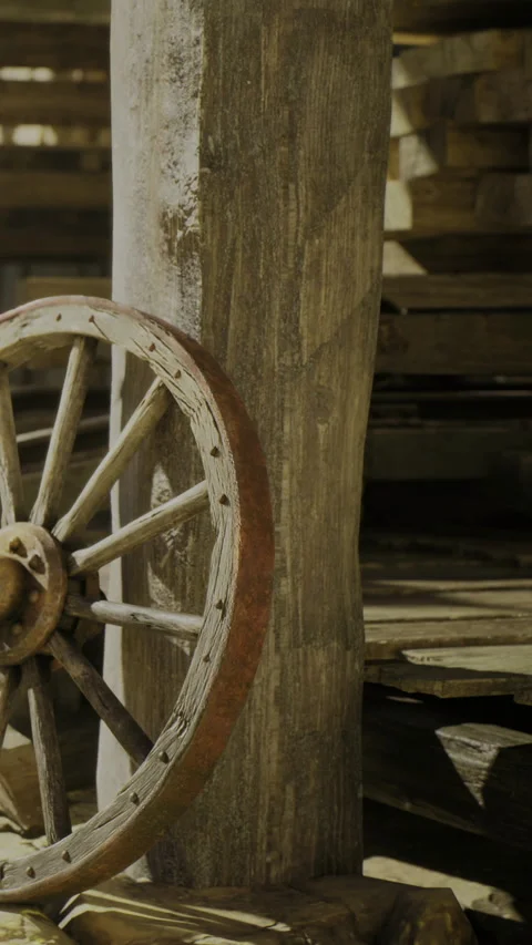 Rustic wooden wheel resting against a weathered post in a sunlit barn Stock Footage 331839225