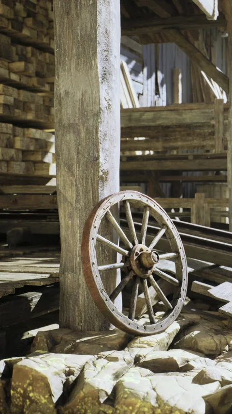Rustic wooden wheel resting against a sturdy post in an old barn setting Stock Footage 331841153
