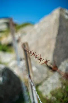 Rusting barbed wire fence border against blue clear sky and rocky outcrop i.. Фото