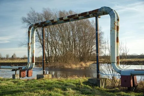 Rusting district heating pipes arched over a flooded field entrance Stock Photos