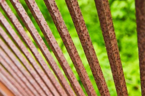 Rusting red and dark brown metal bars in fan formation with blurry green Stock-Fotos
