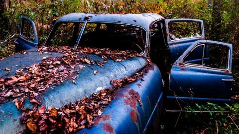 An rusty, abandoned car covered in fallen leaves, found in the woods. Foto stock