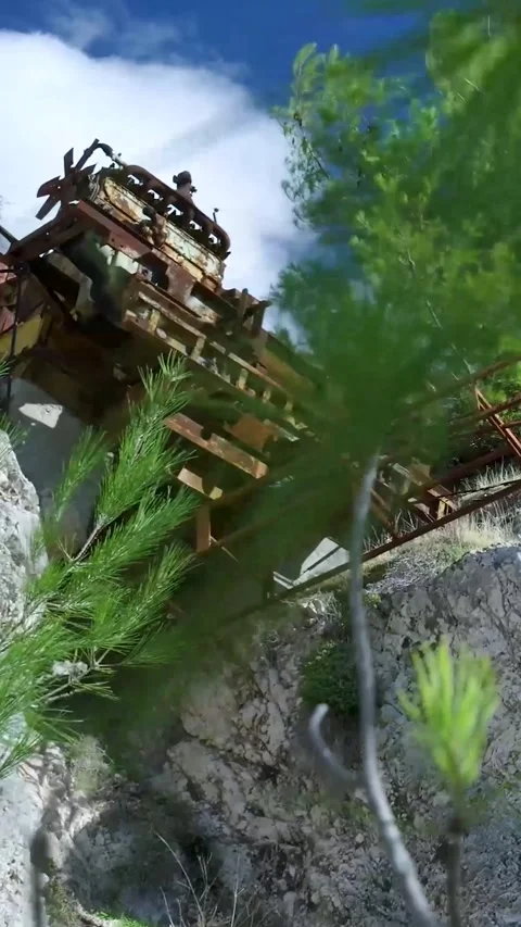 Rusty abandoned mining equipment looming over lush green pine branches Video stock 294964004