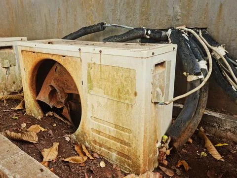 Rusty air conditioner with damaged cables in neglected outdoor area. Equipm.. Foto stock