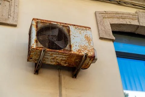 Rusty air conditioning unit mounted on a building facade beside a blue shuttered Stock Photos