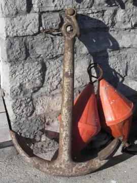 A rusty anchor and two orange conical buoys at the marina Stock Photos