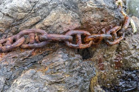 Rusty Anchor Chain Lying on Coastal Shoreline Rocks Texture Stock Photos