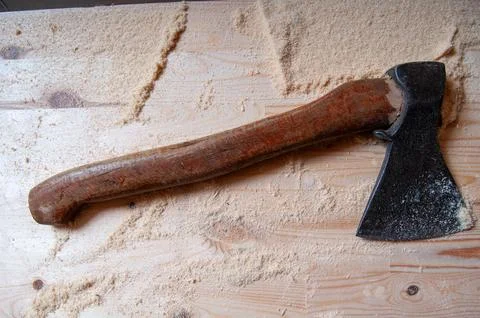 Rusty axe rests on wooden surface. Wood shavings surround the tool. Handle .. Stock Photos