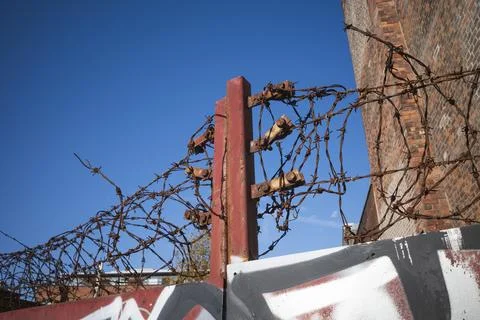 Rusty barbed wire atop a rusty metal gate under a clear blue sky. Stock Photos