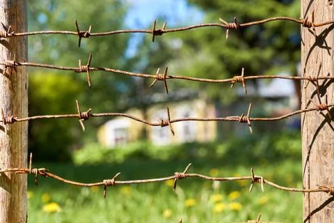 Rusty barbed wires stretched between wooden fence posts with country house on Photos
