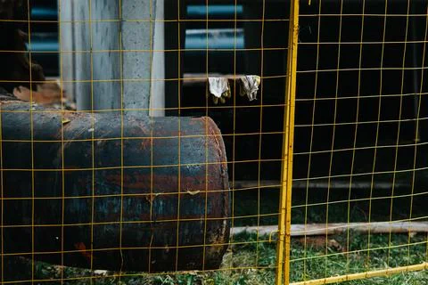 A rusty barrel is located behind a yellow wire fence in a construction area Stock Photos