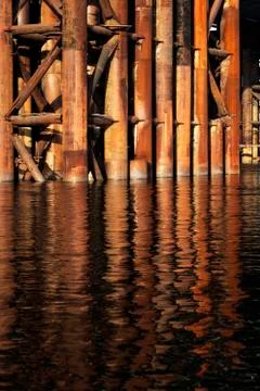 The rusty base of the bridge lowers and is reflected in the water Stock Photos