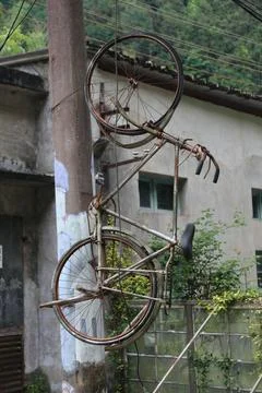 Rusty bicycle frame mounted vertically on a utility pole beside a weathered.. Stock Photos