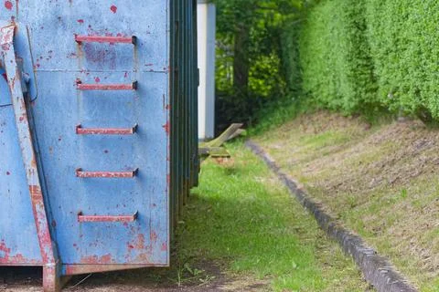 Rusty blue metal container with red handles outdoors near green grass and b.. Photos