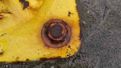 Rusty bolt on yellow surface in industrial area with water around Stock Photos