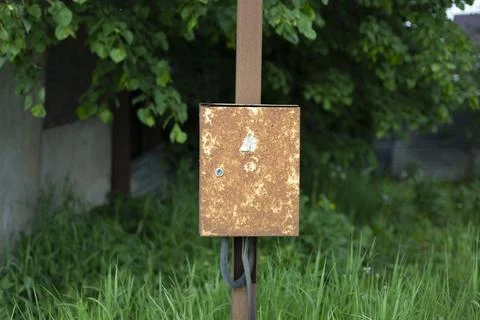 A rusty box on a pole. The box is suspended in the village. Old electrical pa Stock Photos