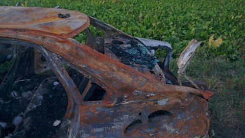 Rusty car after a fire in the background of a green field Stock Footage 114889333
