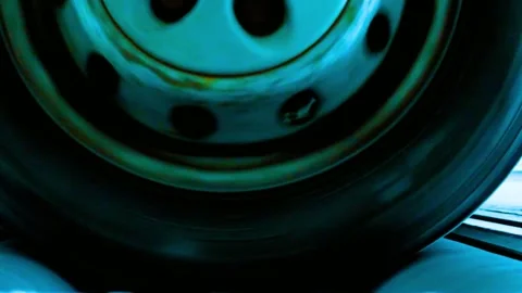 Rusty car wheel spinning fast on roller brake tester in dark garage Stock-Footage 342905514