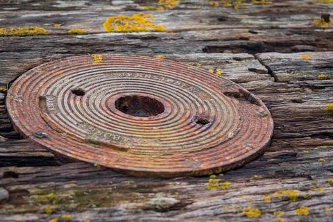 Rusty cast iron disc embedded in weathered timber surface with visible corrosion Stock Photos