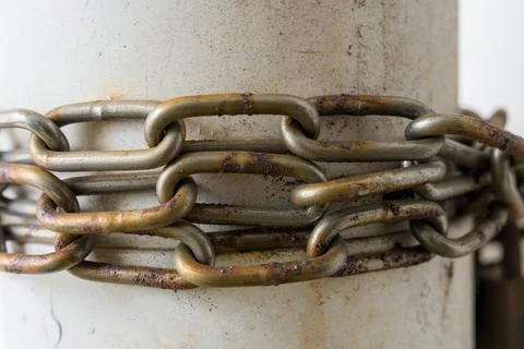 Rusty chain coils tightly around a weathered concrete post Stock Photos