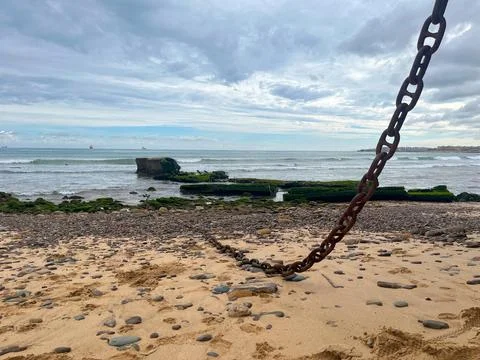 Rusty chain lying on a sandy beach with ocean waves Stock Photos