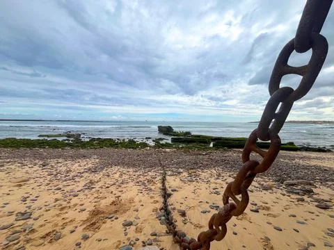 Rusty chain lying on a sandy beach with ocean waves Stock Photos